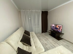 A living room with a beige sofa, a television, and a window with curtains.