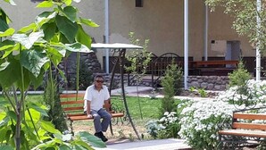 A man sitting on a bench in a garden area with stone walls and greenery. - Daniko (Taraz)