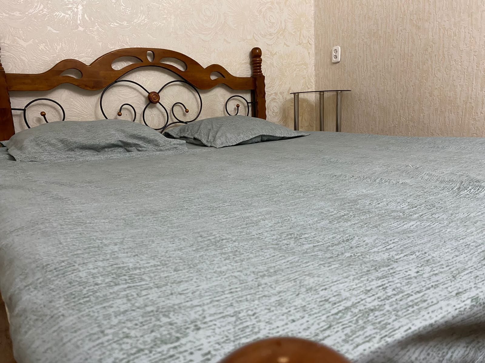 A bed with a wooden headboard and metal frame, a grey blanket, and a bedside table with a lamp.