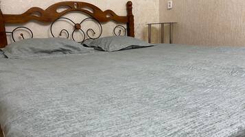 A bed with a wooden headboard and metal frame, a grey blanket, and a bedside table with a lamp.