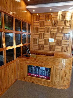 A reception desk with a wooden design, a glass display case, and a wall with a geometric pattern. - The Grand Madhushala Shimla (Shimla)