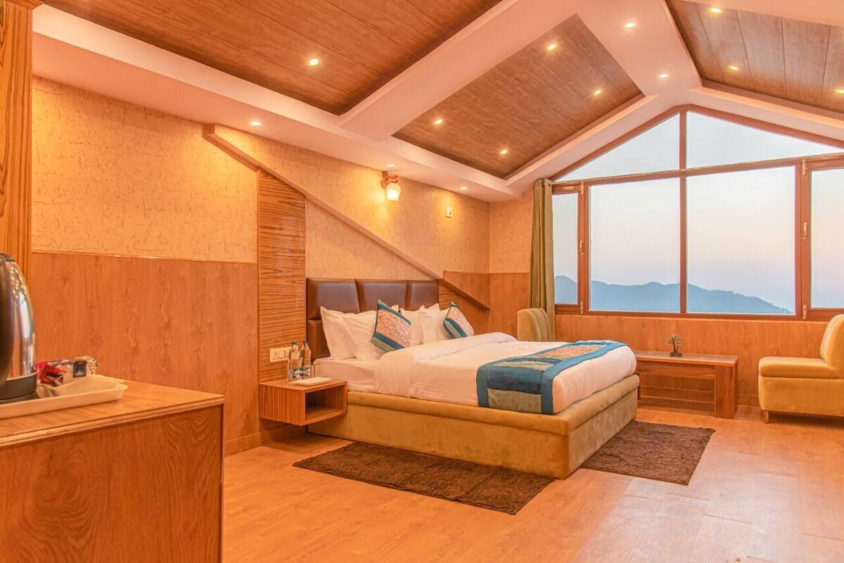 A modern bedroom with a large bed, wooden walls, a skylight, and a view of the mountains.