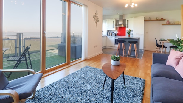 Un appartamento moderno con un balcone, una cucina e un soggiorno con divano e tavolino.