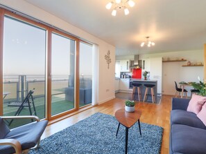 A modern apartment with a balcony, a kitchen, and a living area with a sofa and a coffee table. - Flat 19 By The Beach (Harwich)