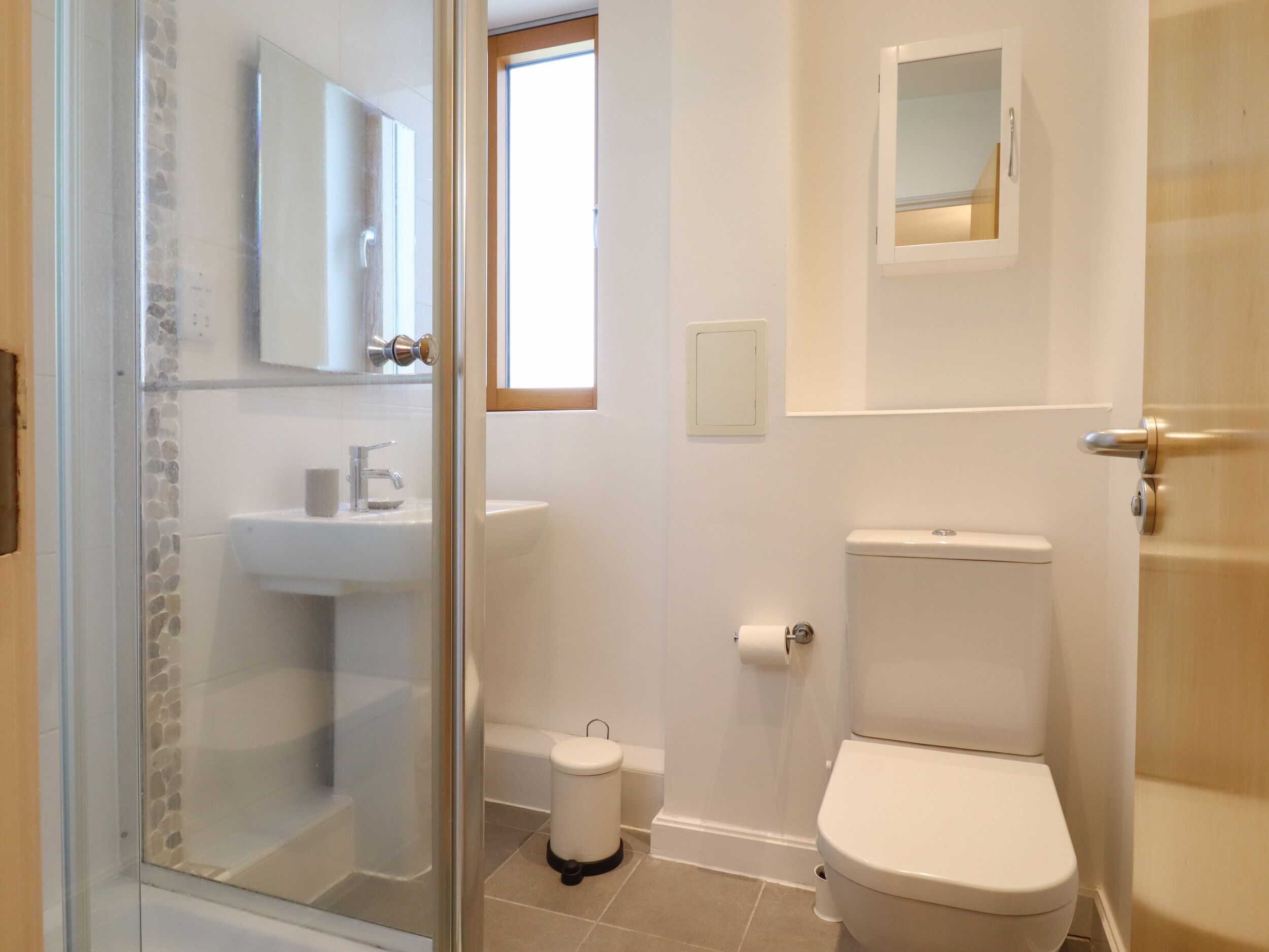 A bathroom with a glass shower enclosure, a sink, a toilet, and a small window.