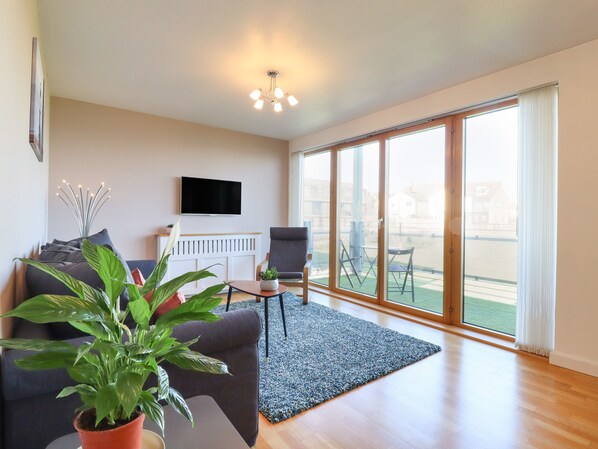 A modern living room with a sofa, a coffee table, a TV, and a large sliding glass door leading to an outdoor area.