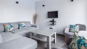 A modern living room with a grey sofa, a coffee table, and a TV mounted on the wall.