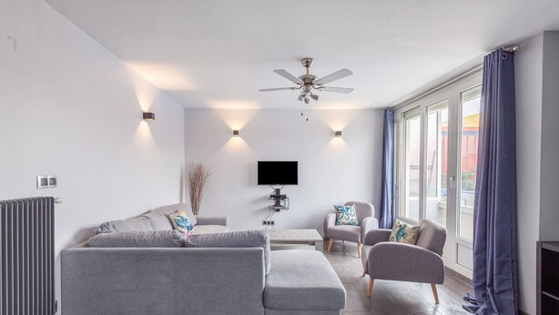 A modern living room with a grey sofa, a small table, a TV, and a ceiling fan.