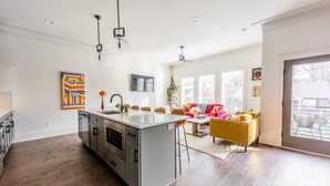 Une cuisine moderne dot ée d’un îlot central, d’un coin repas avec un canapé jaune et d’une grande fenêtre laissant entrer la lumière naturelle.