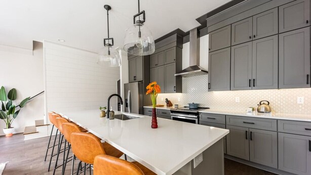 Une cuisine moderne dotée d’un grand îlot central, de meubles gris et de luminaires suspendus.