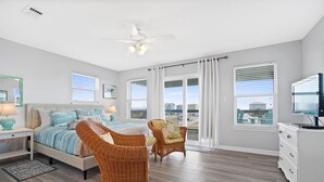 Ein Schlafzimmer mit einem Bett, zwei Korbstühlen, einem Fernseher und Blick auf die Stadt.