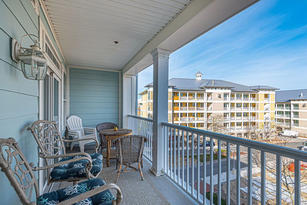 A covered porch with wicker chairs and a small table, overlooking a multi-story building with balconies.