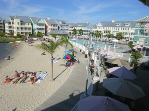 A beach resort with a pool area, beach chairs, umbrellas, and a wooden boardwalk.