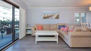 Uma sala de estar com um sofá bege, uma mesa de centro branca e uma pintura de uma praia.