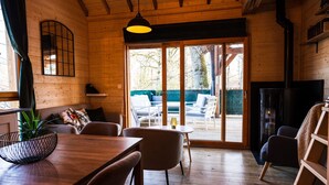 A cozy wooden interior with a dining area, seating, and a view through a glass door to an outdoor patio.