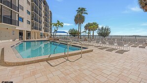 Une piscine entourée de chaises longues et de palmiers, le tout bordé d’un immeuble doté de balcons.