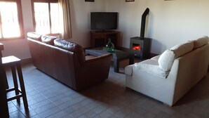 Un soggiorno con un divano, una poltrona bianca, una televisione e un camino a legna.