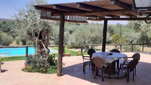 Patio esterno con piscina, pergolato in legno e tavolo con sedie.