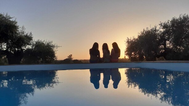 Una piscina con un riflesso limpido, circondata da alberi e un tramonto sullo sfondo.