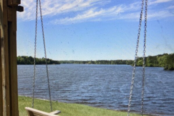 A wooden swing chair overlooking a lake with a clear sky.