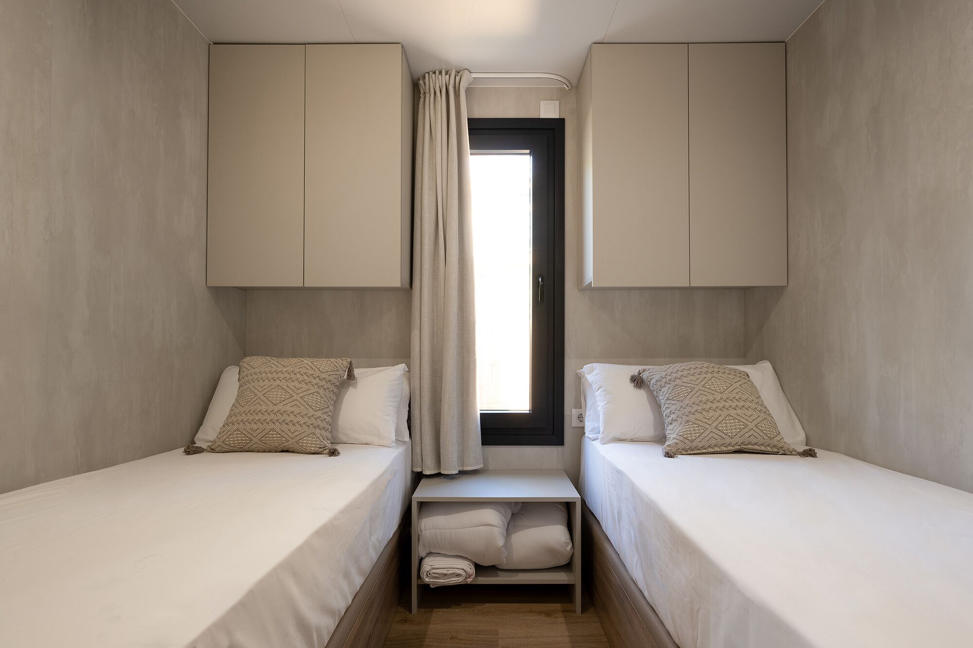 A room with two beds, a small window with curtains, and built-in wardrobes.