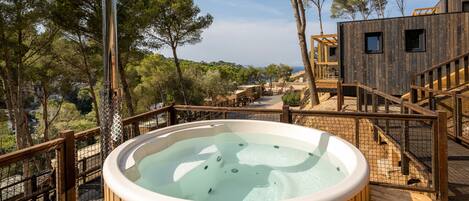 A wooden deck with a hot tub, wooden stairs, and a view of the surrounding trees and landscape.