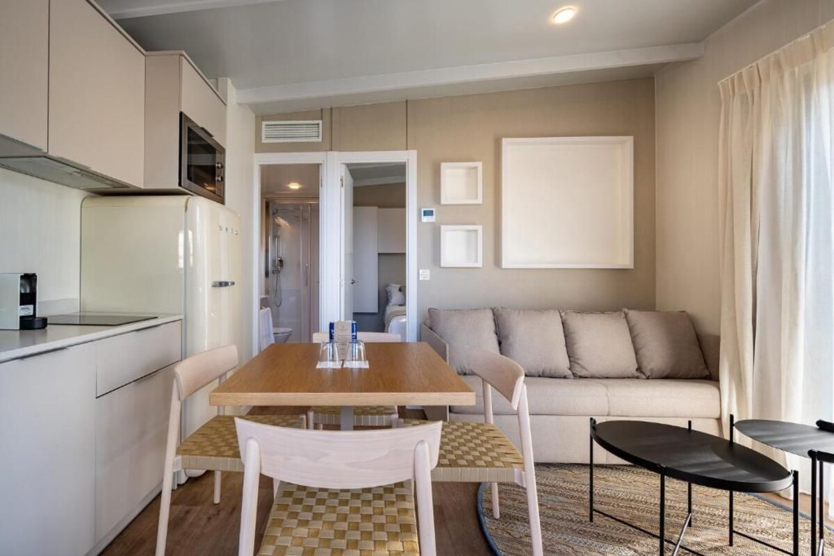 A compact living space with a kitchenette, a dining table with chairs, a sofa, and a small black table.