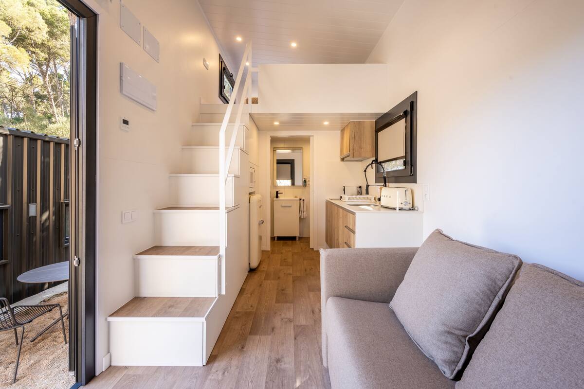 Un espace de vie compact comprenant un escalier menant à une cuisine et un coin repas, un canapé et une petite table avec des chaises.