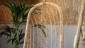 A wicker hanging chair with a white cushion, a potted plant, and a woven ceiling light fixture. - Talaia Plaza Ecoresort (Begur)