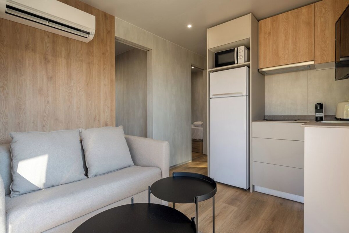 A compact living space with a sofa, a small round table, a kitchenette with a microwave, and a refrigerator.