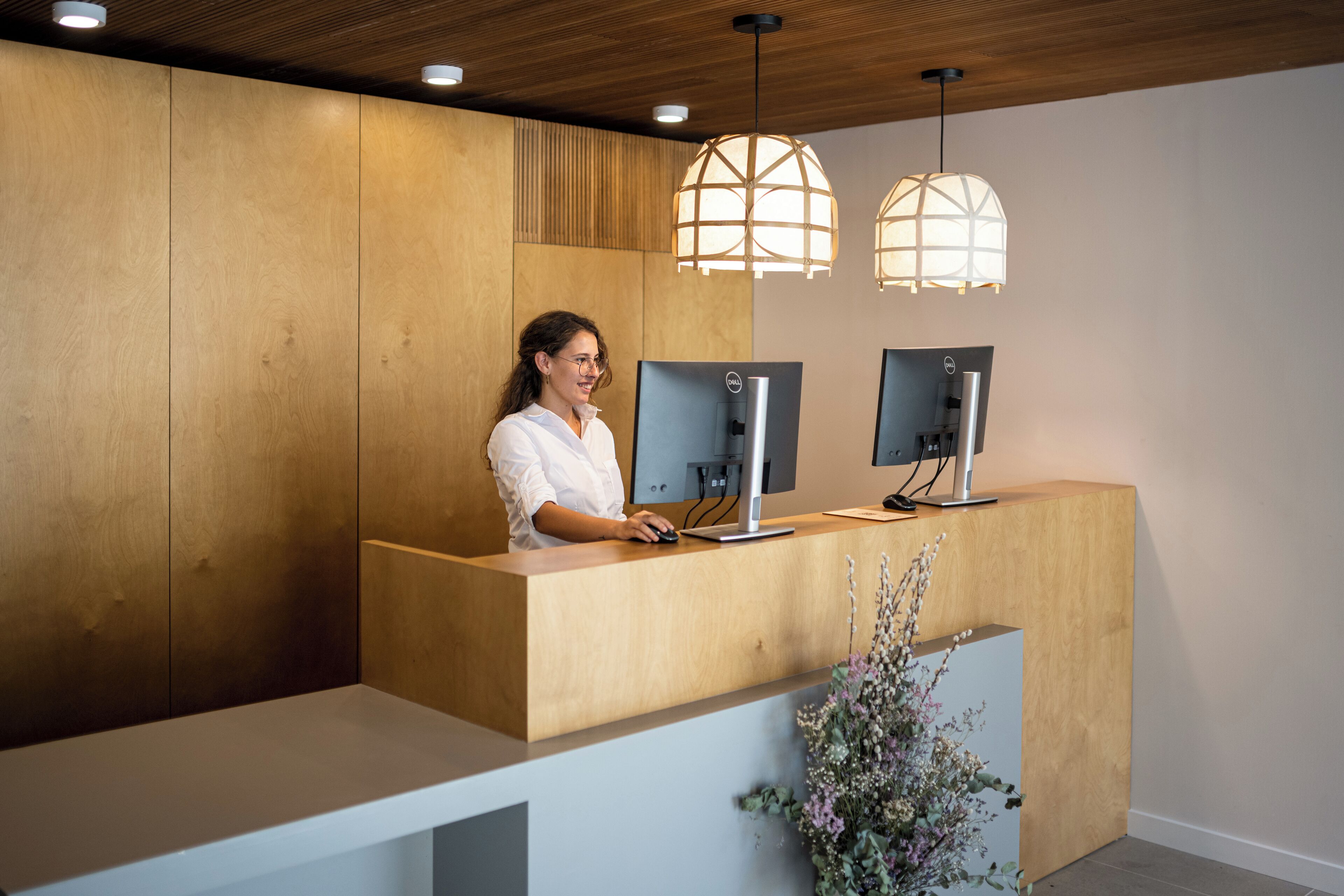 Una recepción con dos monitores, un panel de pared de madera e iluminación colgante.