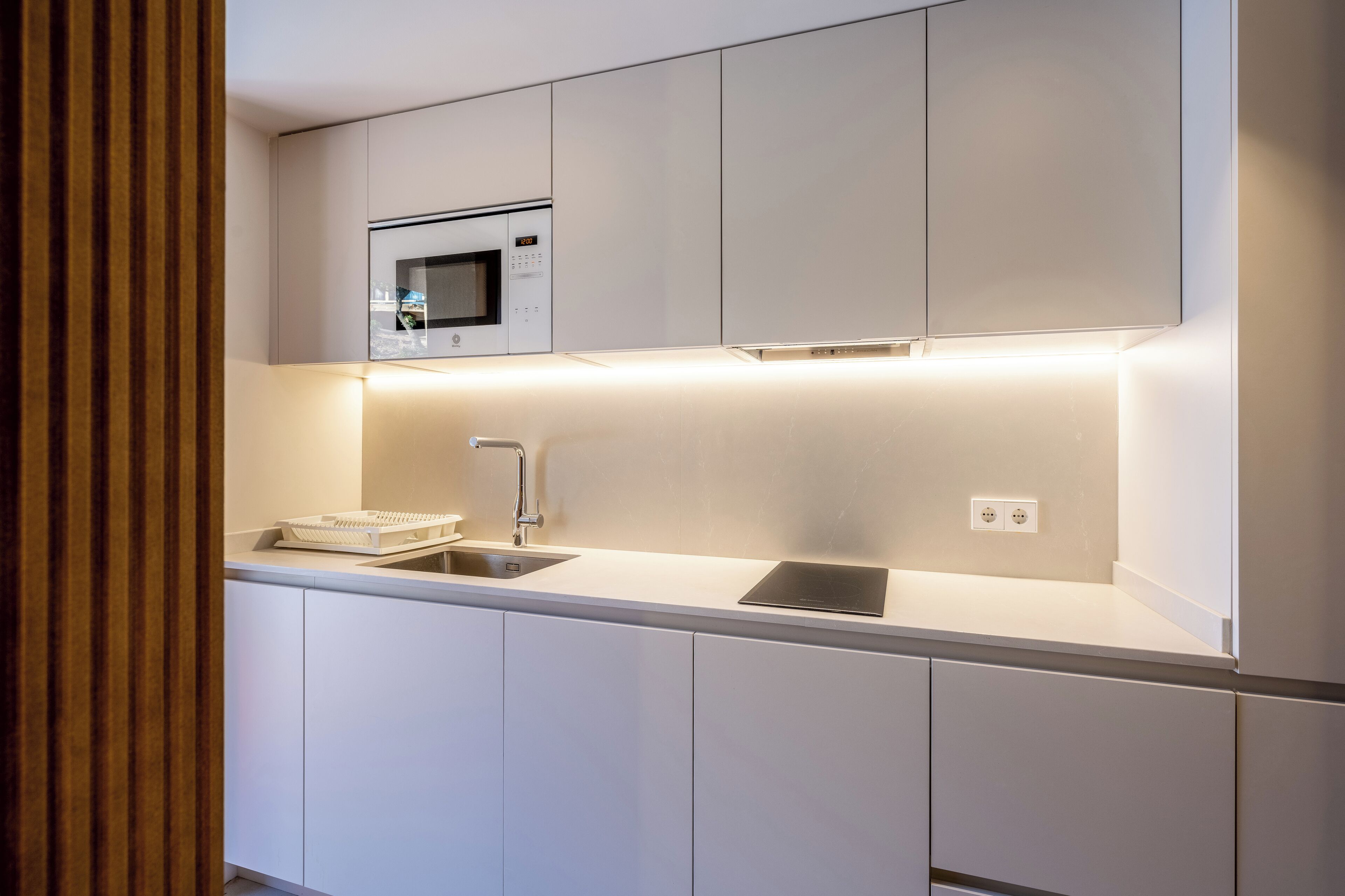 Una cocina moderna con armarios blancos, microondas integrado, un lavabo e iluminación debajo de los gabinetes.
