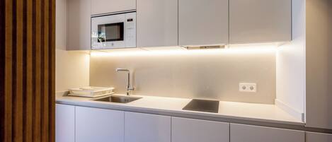 Una cocina moderna con armarios blancos, microondas integrado, un lavabo e iluminación debajo de los gabinetes.
