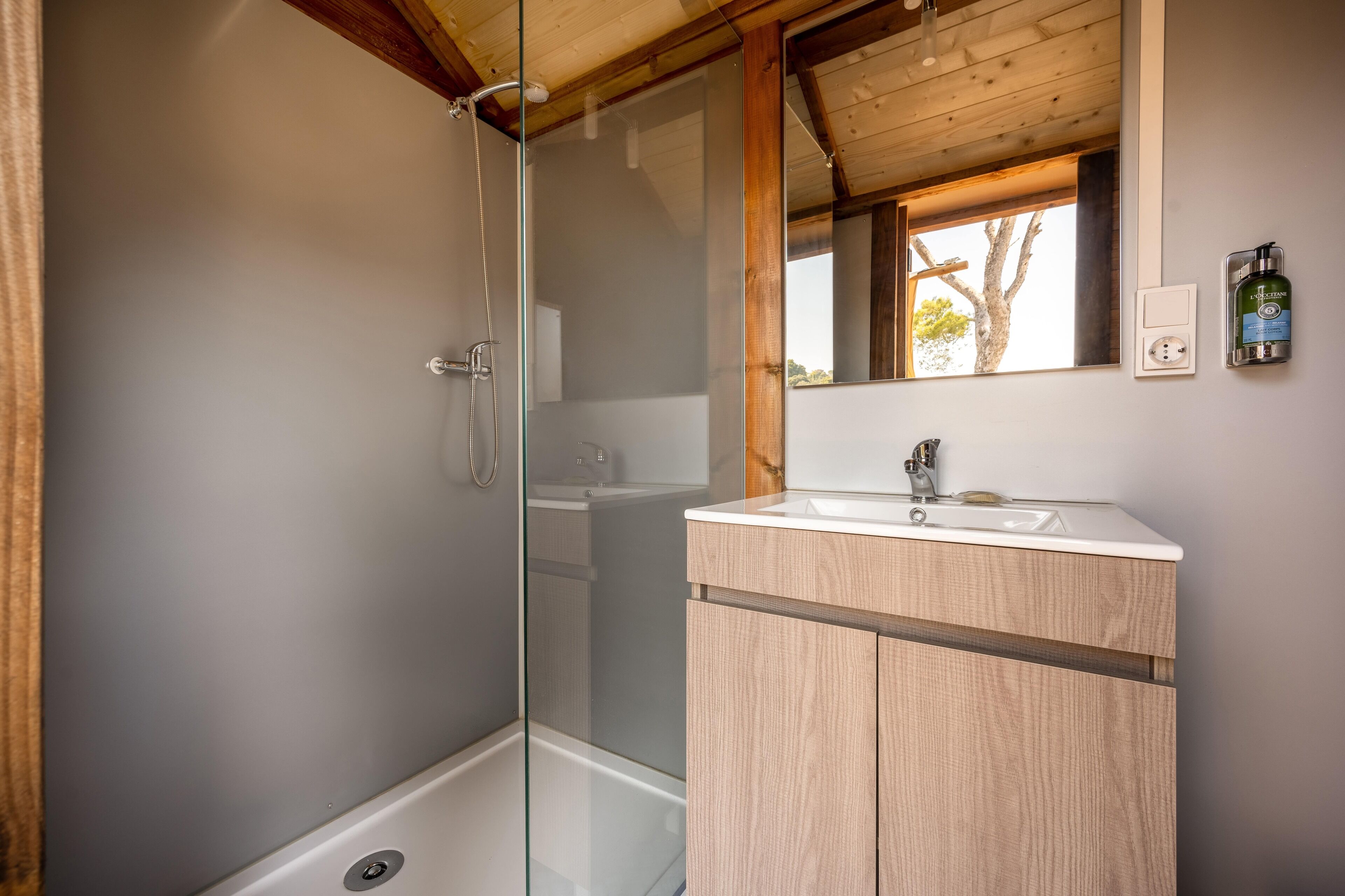 Un bany modern amb dutxa tancada amb vidre, armaris de fusta i un gran mirall sobre el lavabo.