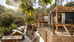 A row of wooden cabins with stone walls, connected by a pathway, surrounded by trees. - Talaia Plaza Ecoresort (Begur)