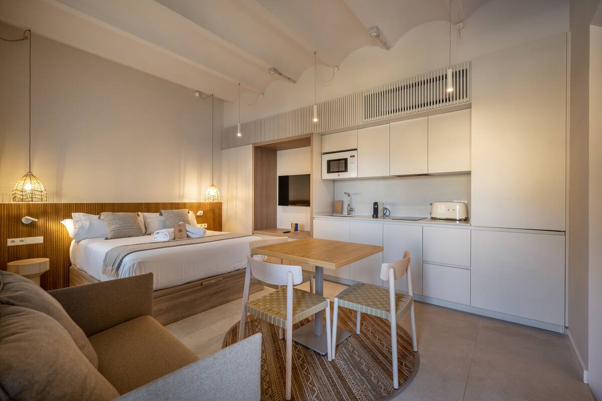 Une chambre d’hôtel moderne équipée d’un lit, de tables de chevet, d’un petit bureau, d’une chaise, d’un canapé et d’un coin cuisine avec un four à micro-ondes et un grille-pain.