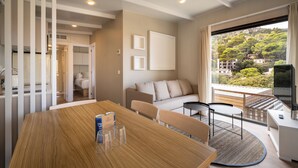A modern hotel room with a dining area, a sofa, and a balcony with a view of the city. - Talaia Plaza Ecoresort (Begur)