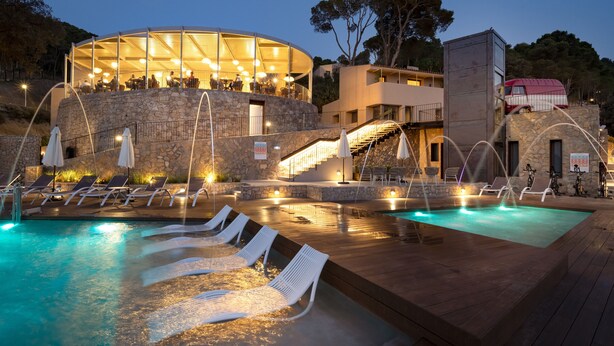 A pool area with lounge chairs, a restaurant with outdoor seating, and a stone building with a staircase. - Talaia Plaza Ecoresort (Begur)