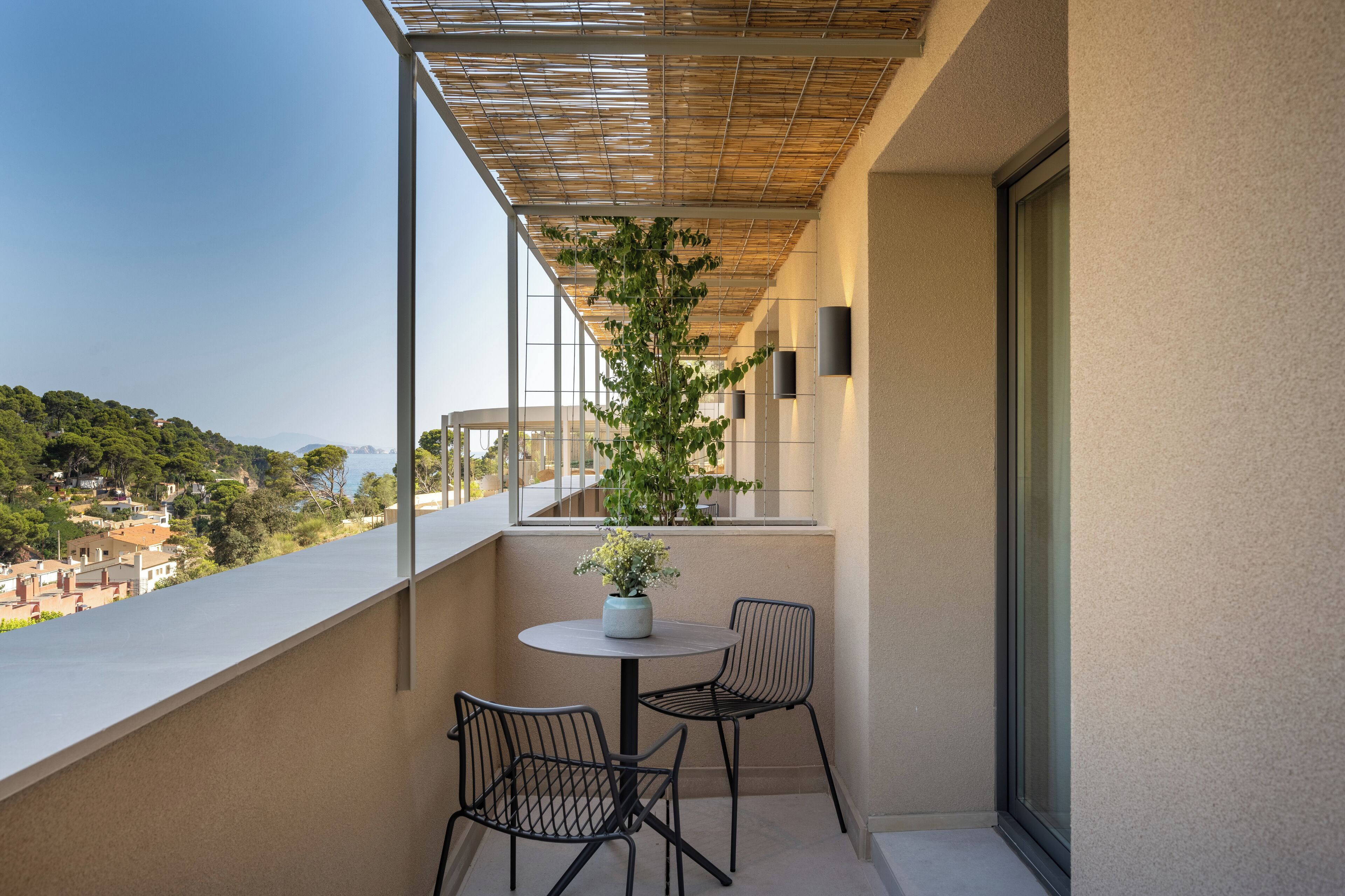A balcony with a potted plant, two chairs, and a view of a hillside.