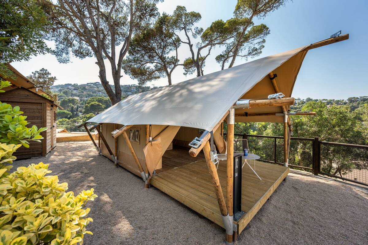 Une tente dotée d’une terrasse en bois, entourée d’arbres et offrant une vue sur la campagne.