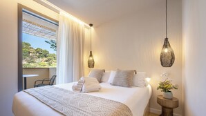 A hotel room with a large bed, a small table, a chair, a bedside table with a vase, and a view of the outdoors. - Talaia Plaza Ecoresort (Begur)