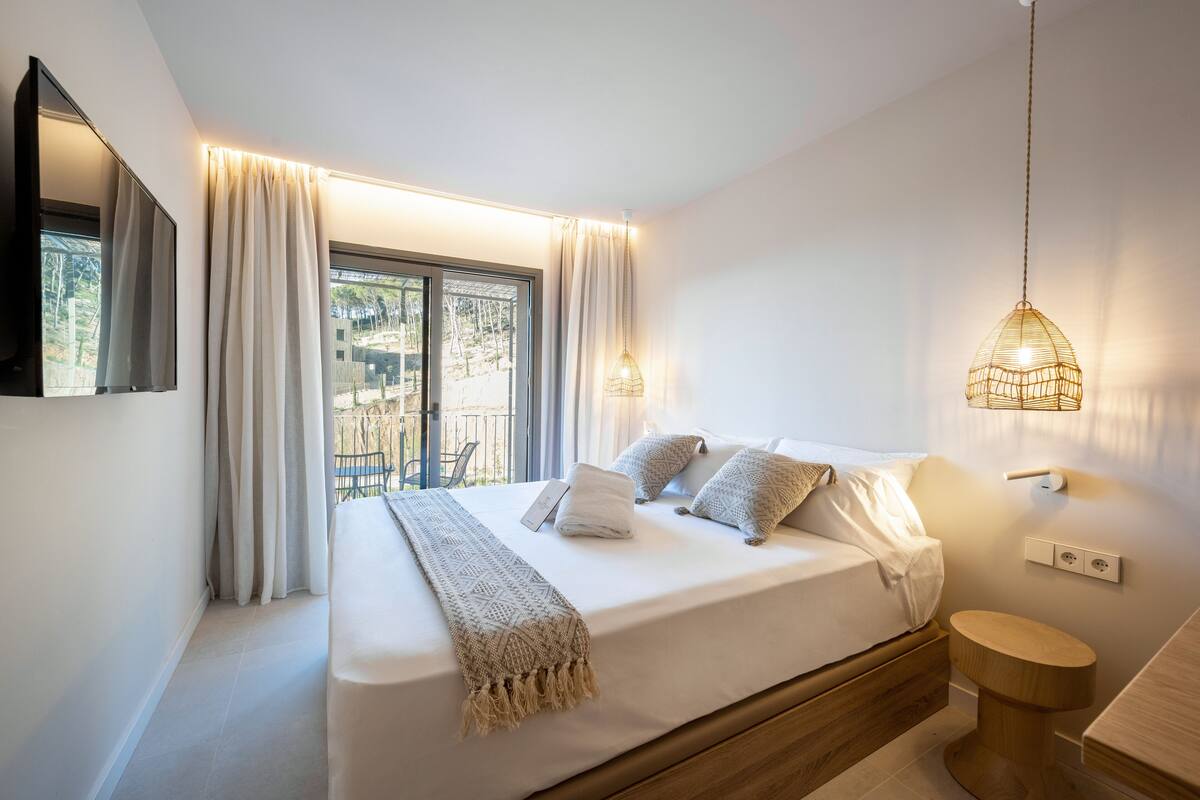 Une chambre à coucher moderne avec un lit, des rideaux, une lampe de chevet et une vue sur l’extérieur.