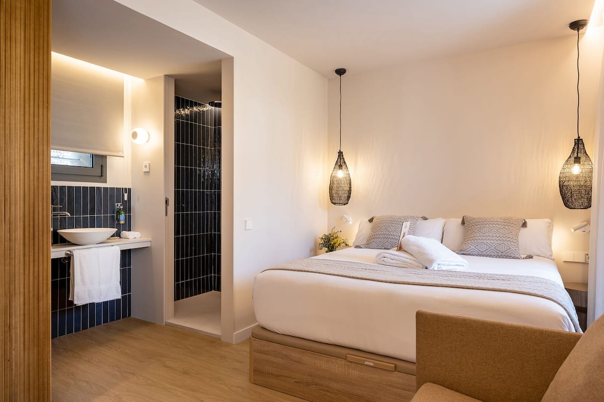 Une chambre à coucher comprenant un lit, des lampes de chevet, une table de nuit, un miroir et une salle de bain avec un lavabo et un porte-serviettes.