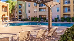 A pool area with lounge chairs, a wooden pergola, and a multi-story building with balconies in the background. - Surprise Ground Floor Condo with 2 Private Courtyards! Heated Community Pool! (Surprise)