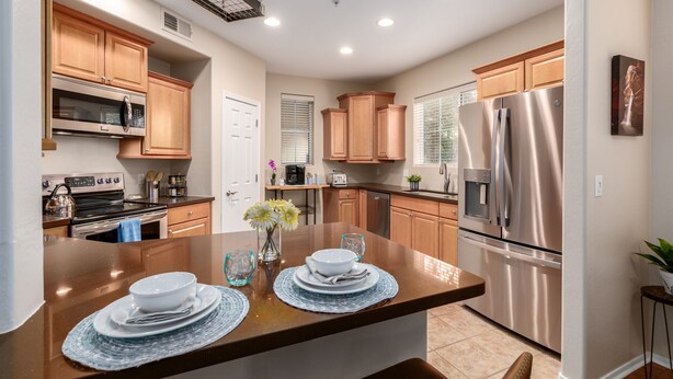 A modern kitchen with wooden cabinets, stainless steel appliances, and a central island with a vase of flowers. - Surprise Ground Floor Condo with 2 Private Courtyards! Heated Community Pool! (Surprise)