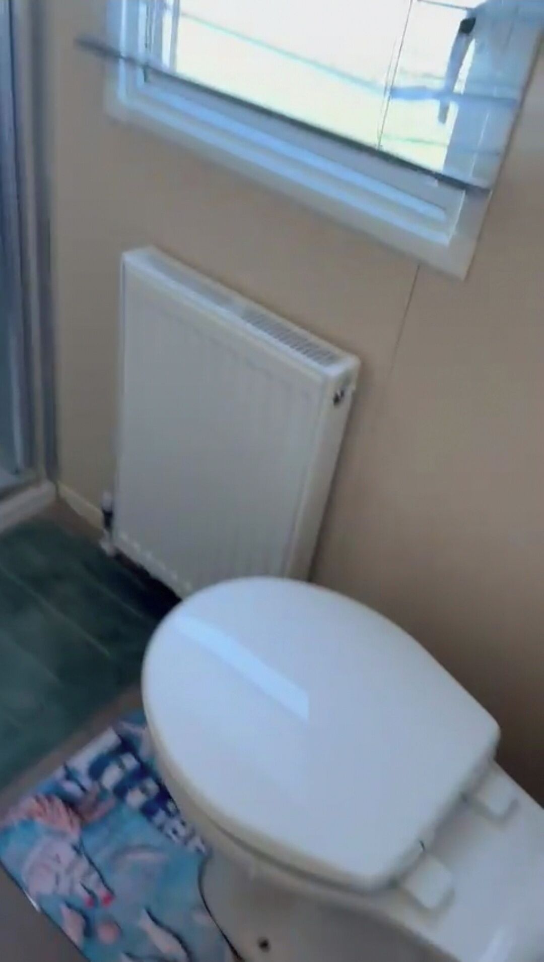 A small bathroom with a toilet, a radiator, and a window.