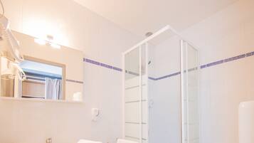 Une salle de bain avec un lavabo blanc, un miroir et des toilettes, une douche en verre et un carrelage à motifs à carreaux.