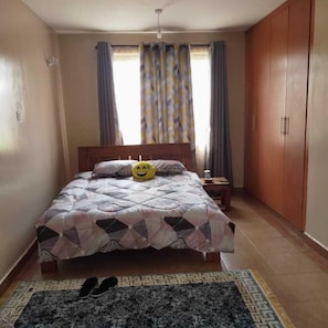A bedroom with a bed, a nightstand, a wardrobe, and a patterned rug.