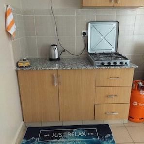 A kitchen with a gas stove, a kettle, and a gas cylinder.