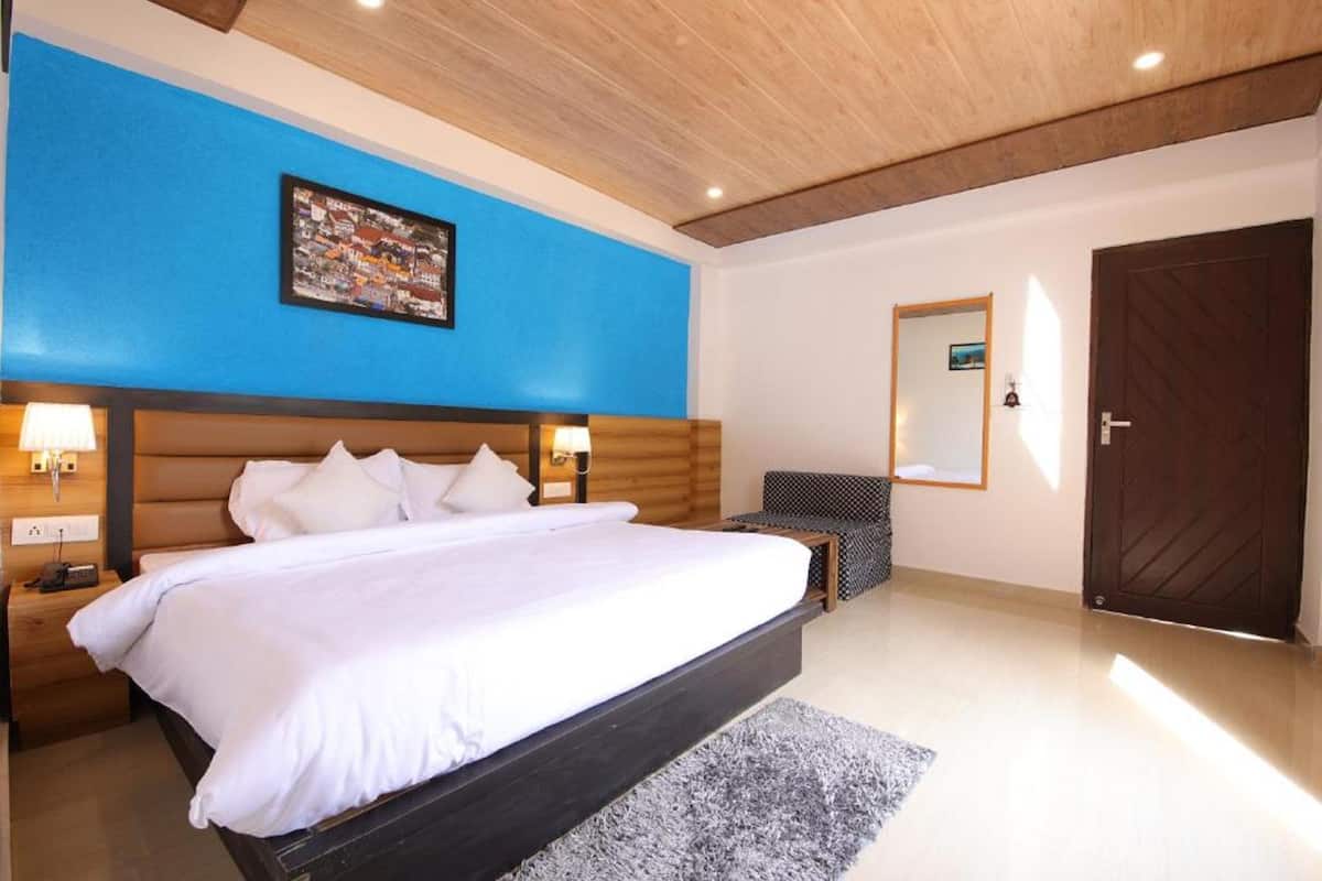 A large bed with white linens, a wooden headboard, bedside lamps, a blue accent wall, a framed picture, a mirror, and a dark wooden door.